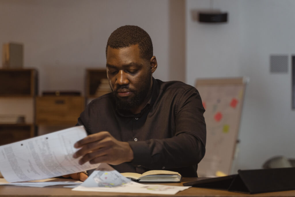 Person with dark skin tone looks over paperwork at their desk.