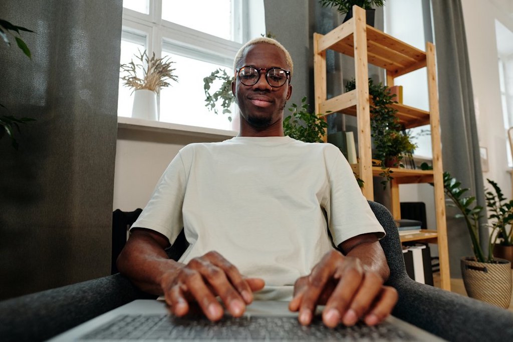 Person with dark skin tone smiles to themselves as they type at their laptop.
