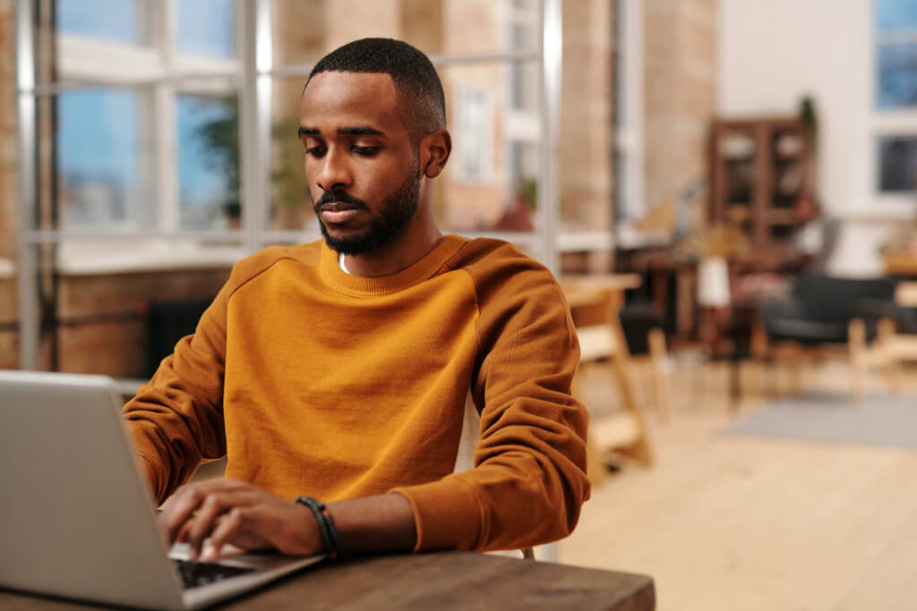 Person with dark skin tone works away at their laptop at a co-working space.