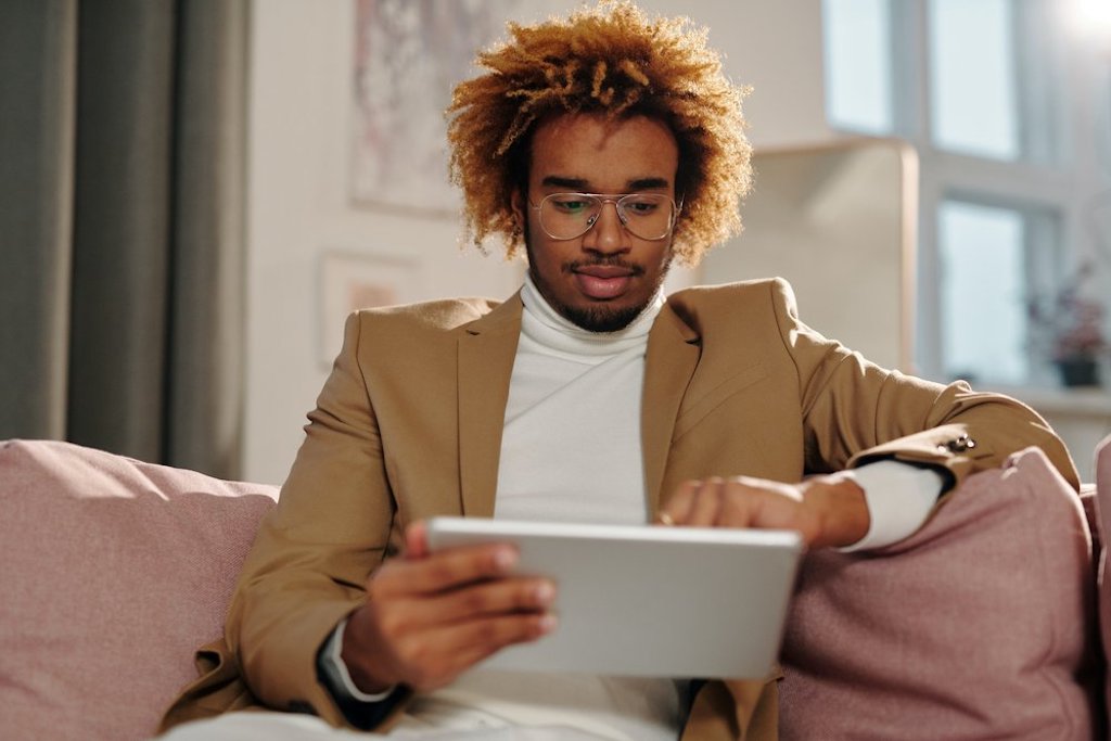 Person with dark skin tone looks at their tablet on a couch.